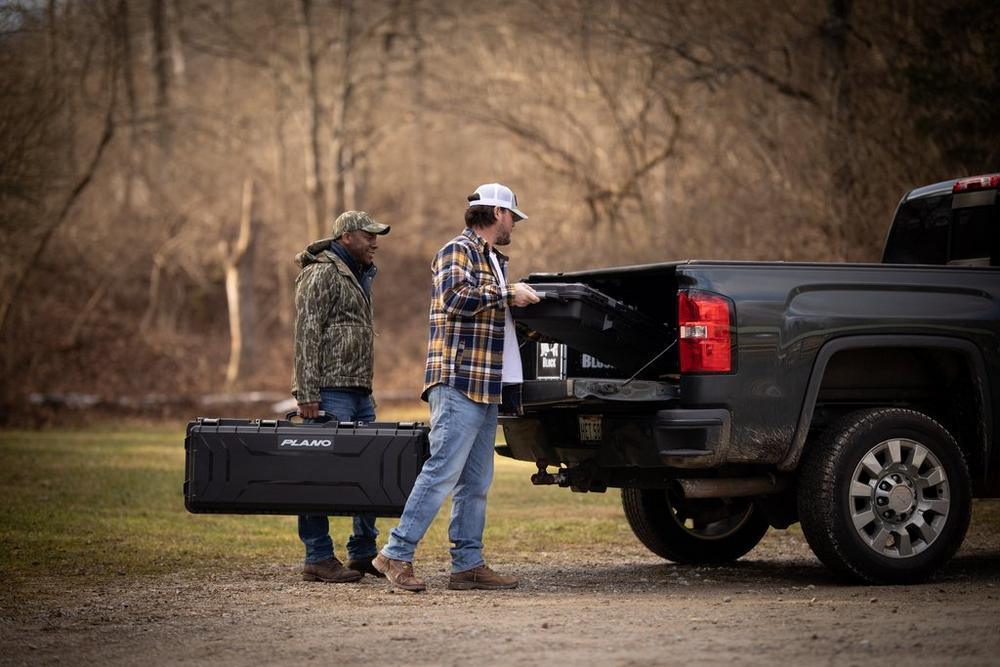 Two men loading Plano Archery Field Locker bow case into pickup truck outdoors