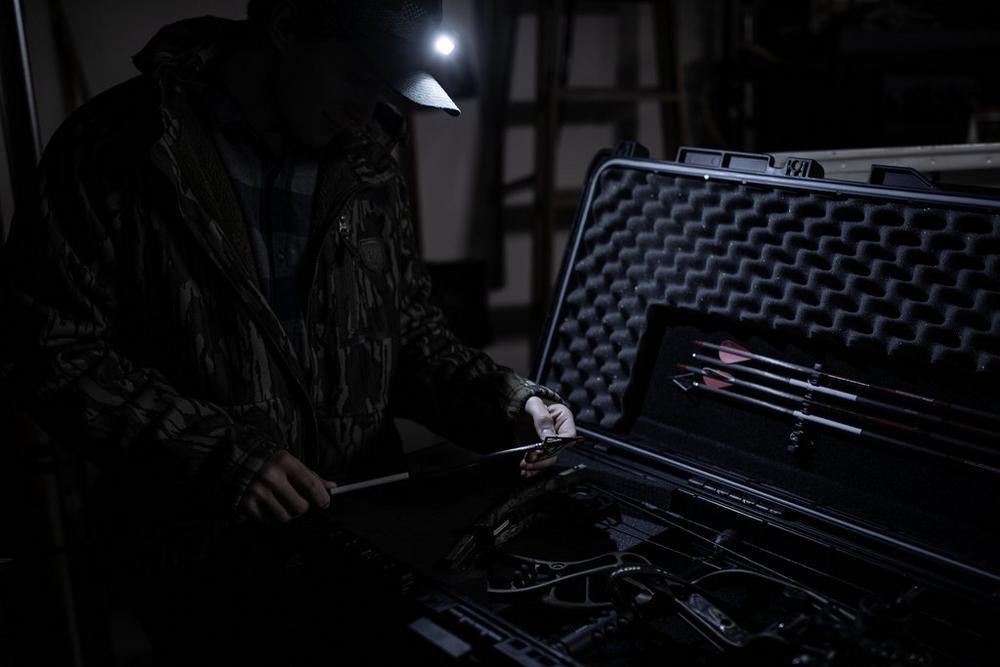 Hunter with headlamp opening Plano Archery Field Locker bow case with arrows and bow inside
