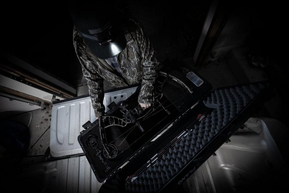 Person packing compound bow in Plano archery field locker bow case in garage