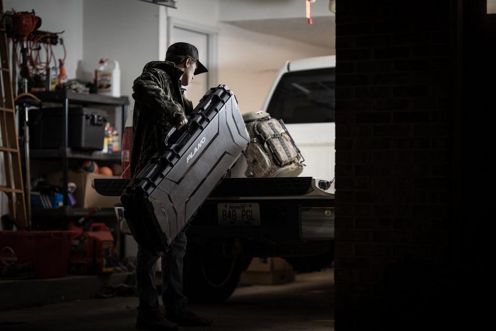 Man loading Plano archery field locker bow case into truck bed in garage