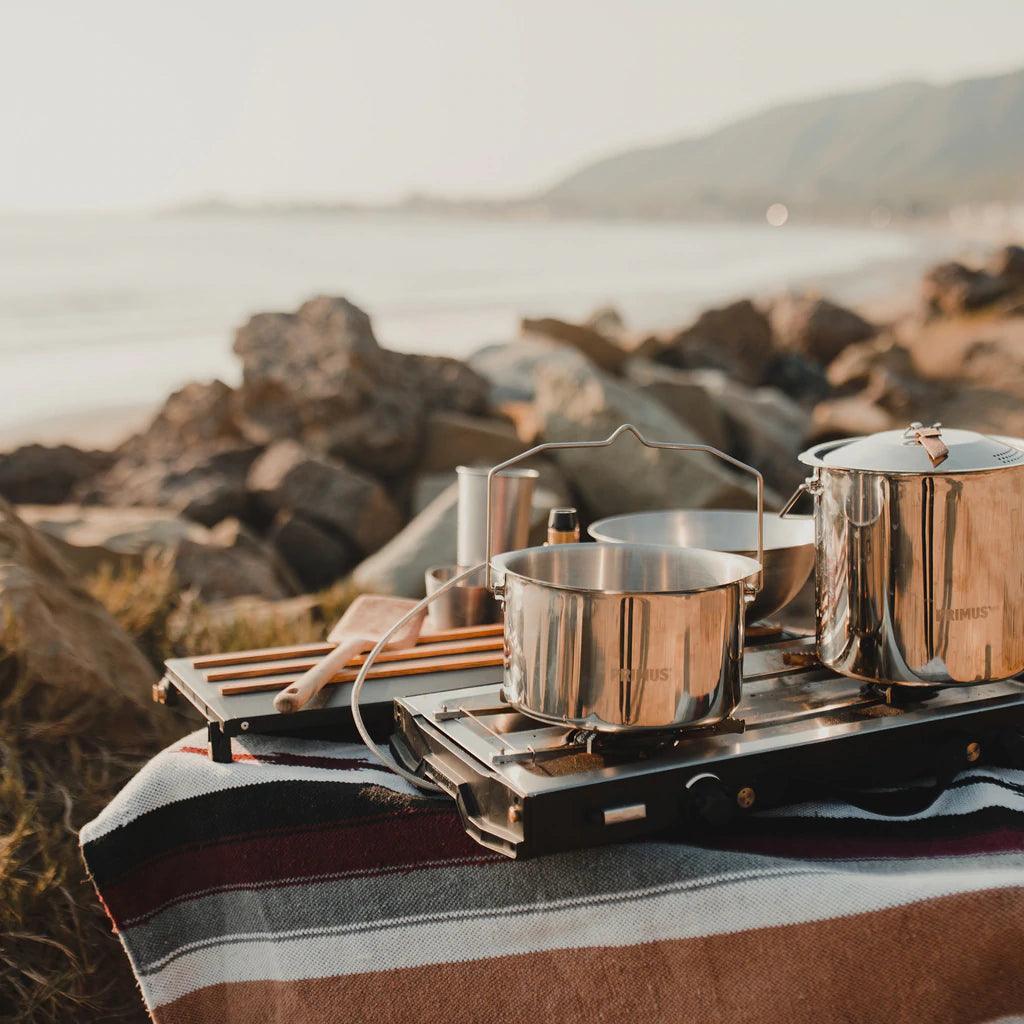 Primus Alika camping stove with pots on a striped blanket by the rocky beach