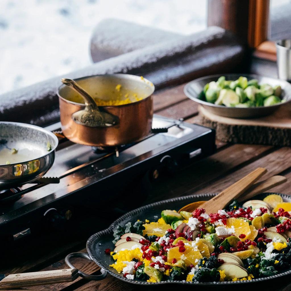 Primus Alika stove on wooden table with copper pot and colorful salad outdoors