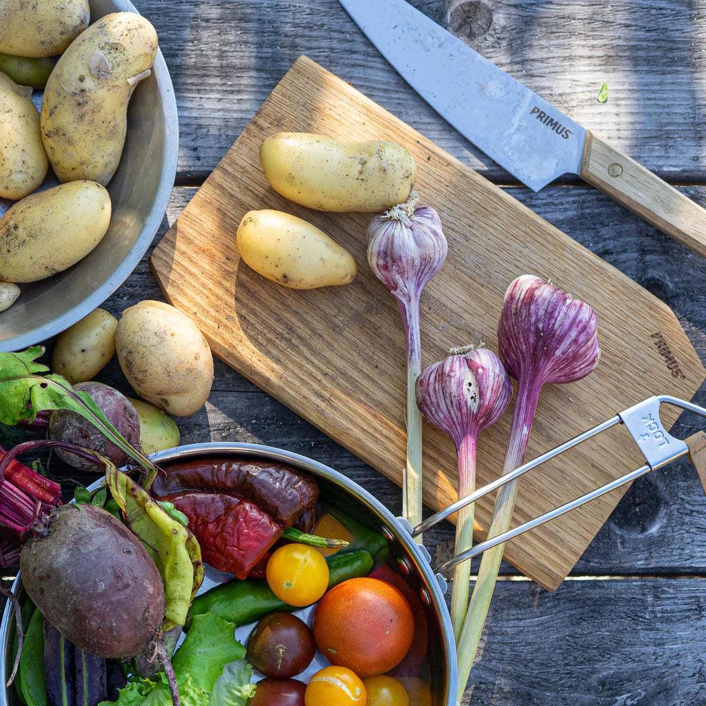 Primus campfire cutting set with knife, cutting board, potatoes, garlic, and fresh vegetables