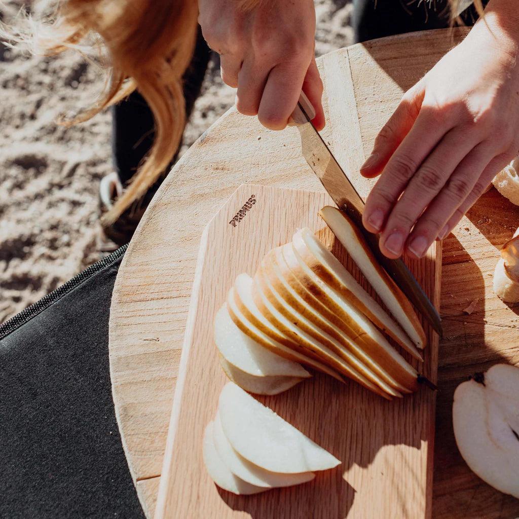 Slicing pear on Primus wooden cutting board outdoors, camp kitchen setup
