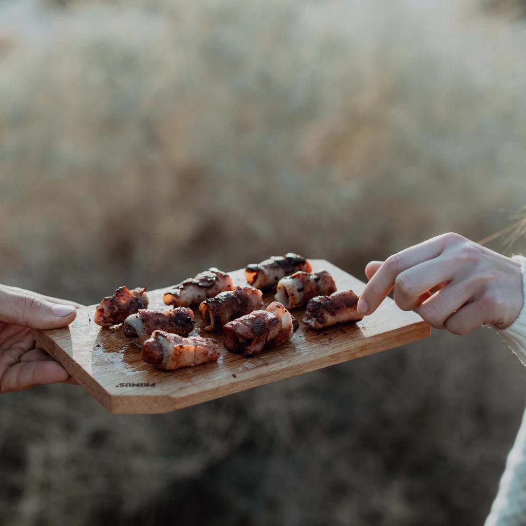 Grilled meat appetizers served on a wooden cutting board outdoors, Primus camping gear