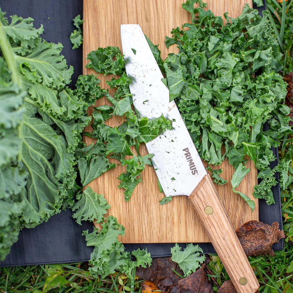 Primus campfire knife with wooden handle cutting fresh kale on bamboo board outdoors