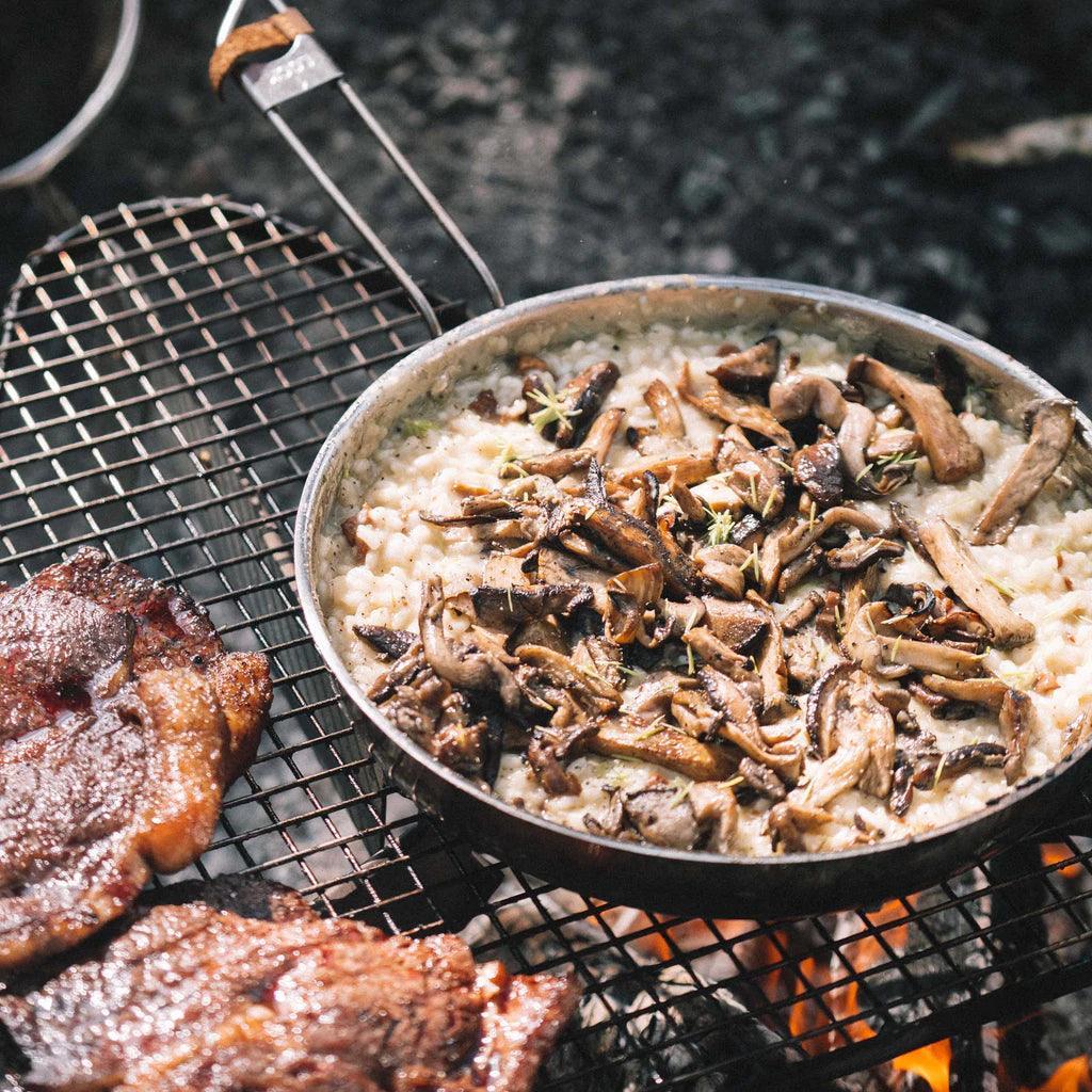 Primus campfire frying pan cooking mushroom risotto and grilled meat over open flame outdoors