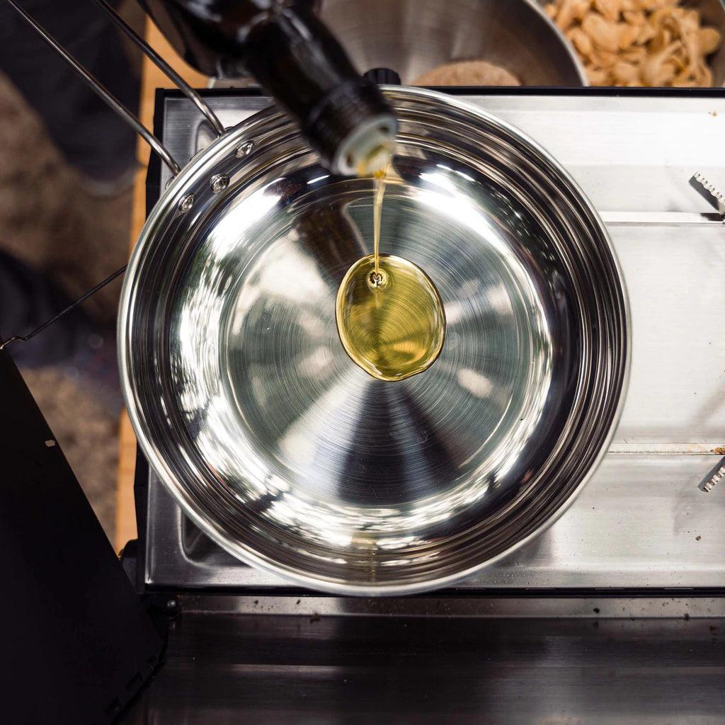 Pouring oil into a stainless steel Primus campfire frying pan on a stove outdoors