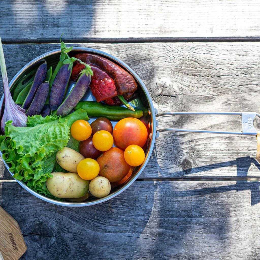 Primus Campfire frying pan with assorted fresh vegetables on wooden outdoor table