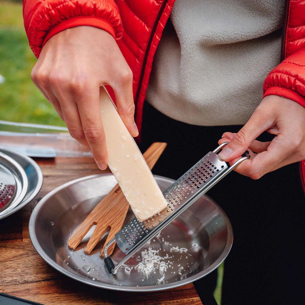 Hand grating cheese into a Primus stainless steel camping plate outdoors