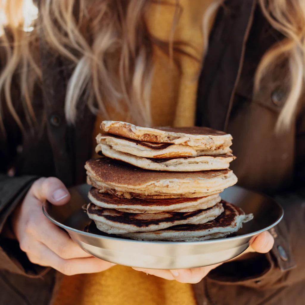 Stack of pancakes on stainless steel camping plate held outdoors