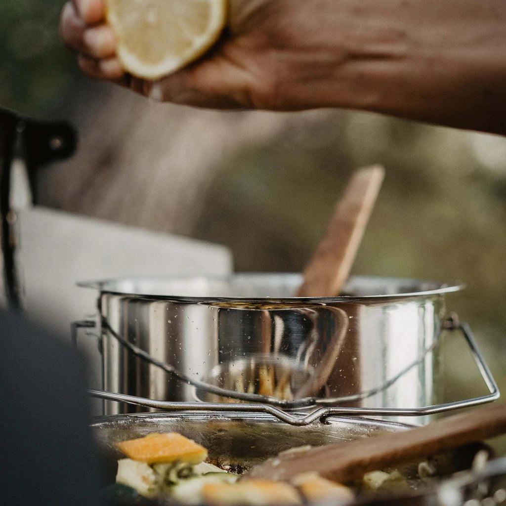 Hand squeezing lemon over Primus stainless steel campfire pot outdoors