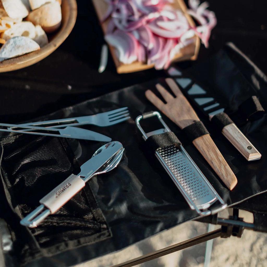 Primus campfire prep set with utensils, grater, and sliced bread on outdoor table