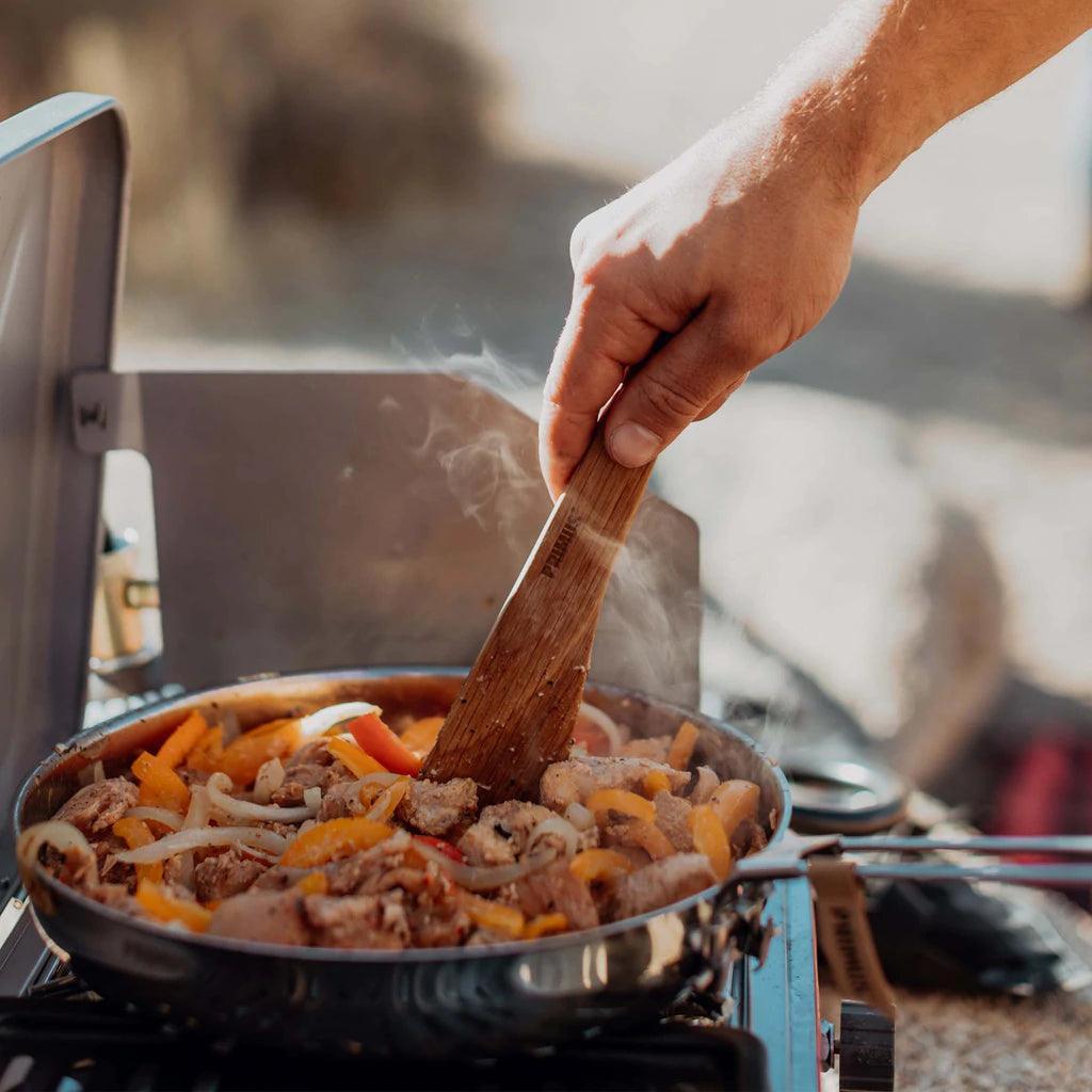 Hand cooking meat and vegetables in skillet on portable camp stove outdoors