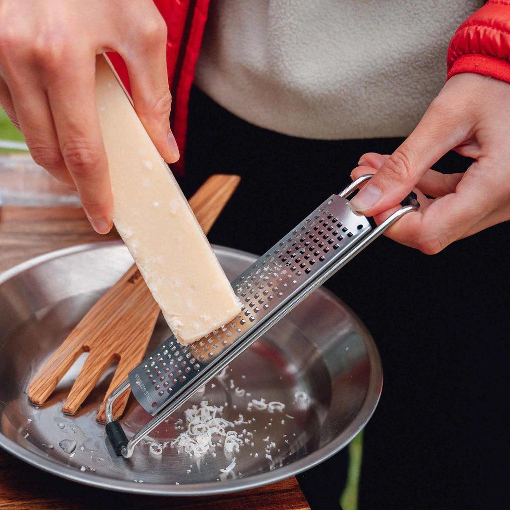 Grating cheese with stainless steel Primus campfire prep set over a metal bowl outdoors