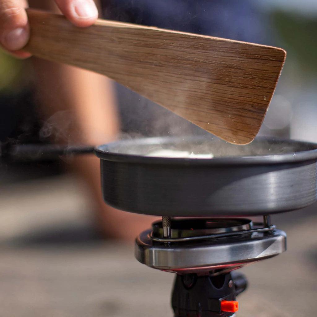 Hand stirring pan on portable camping stove with wooden spatula outdoors