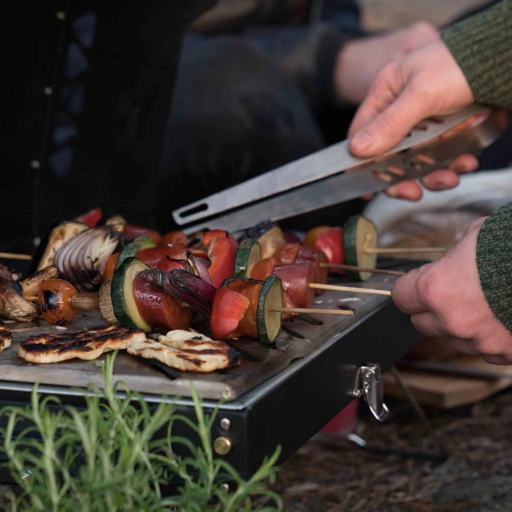 Grilling vegetable skewers with Primus campfire tongs on outdoor portable grill