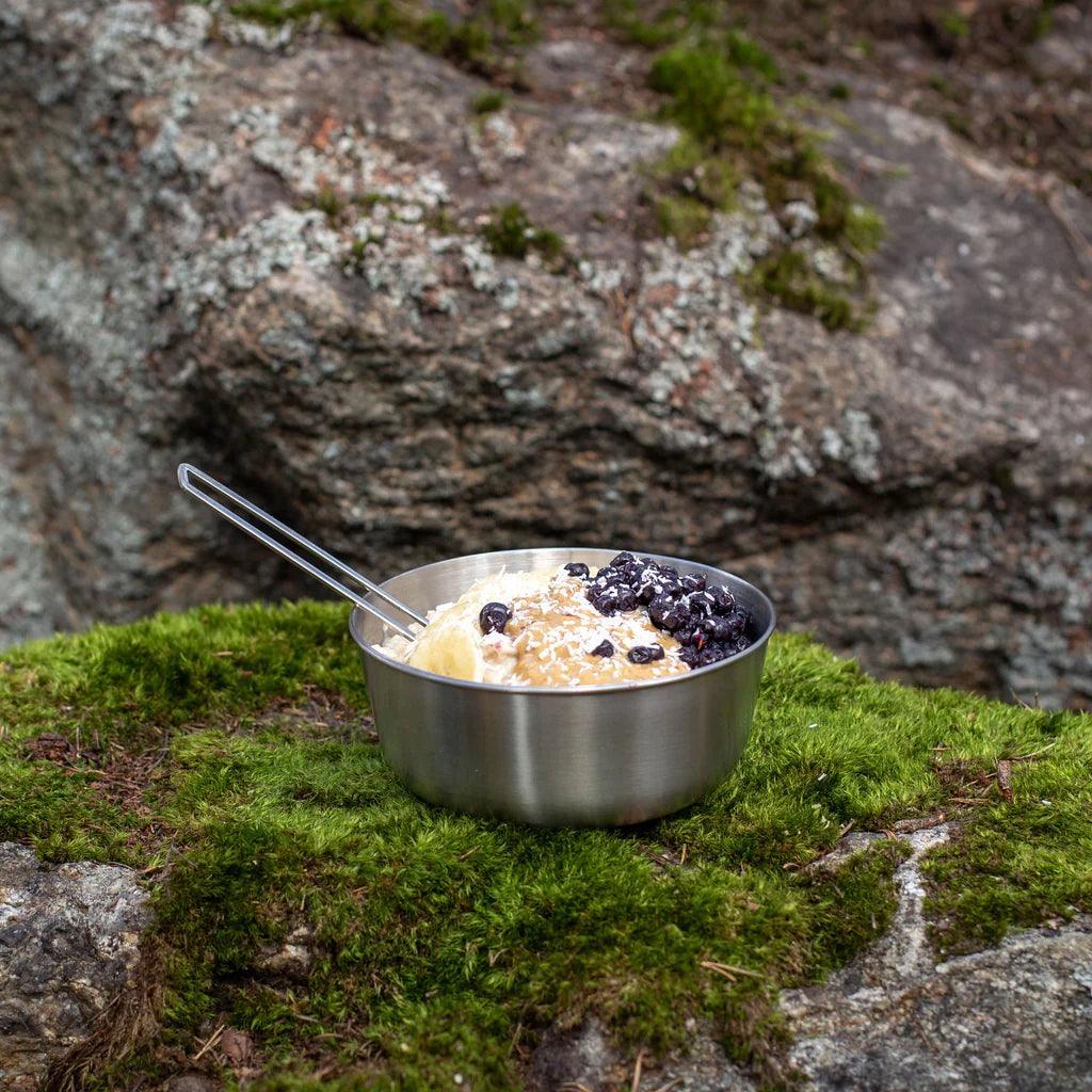 Primus stainless steel campsite bowl with food on mossy rock outdoors