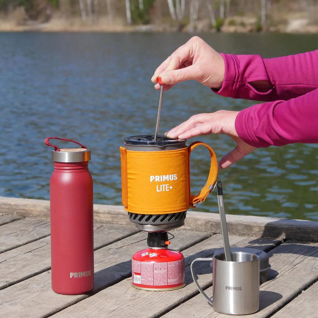 Primus Lite+ camping coffee press and gear on dock by lake, outdoor adventure scene