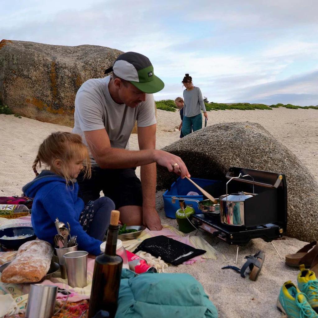 Family cooking on portable camp stove with Primus cookset on sandy beach campsite