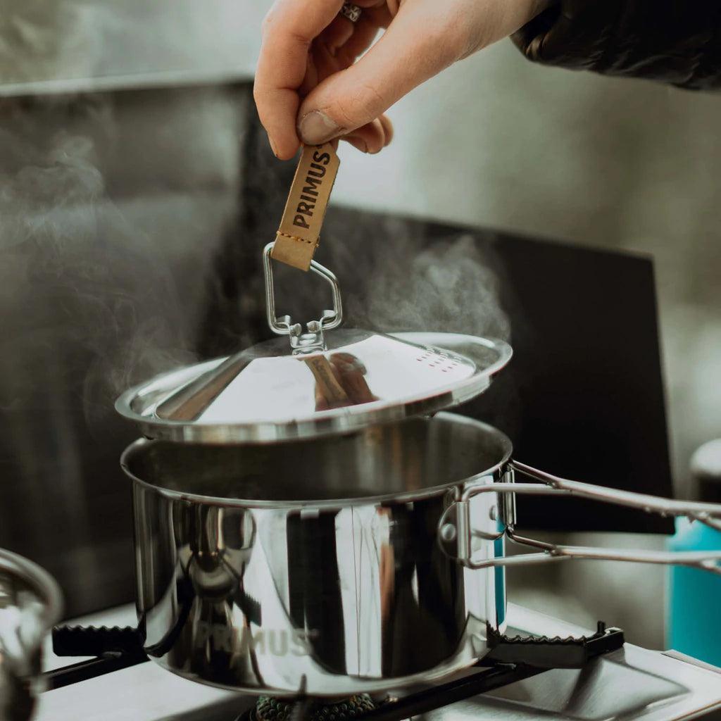 Hand lifting lid from steaming Primus stainless steel campsite cookset on stove