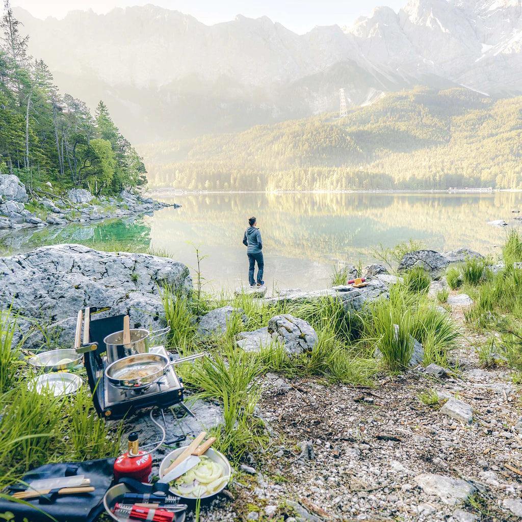 Primus campsite cookset on rocky lakeside with person enjoying scenic mountain view