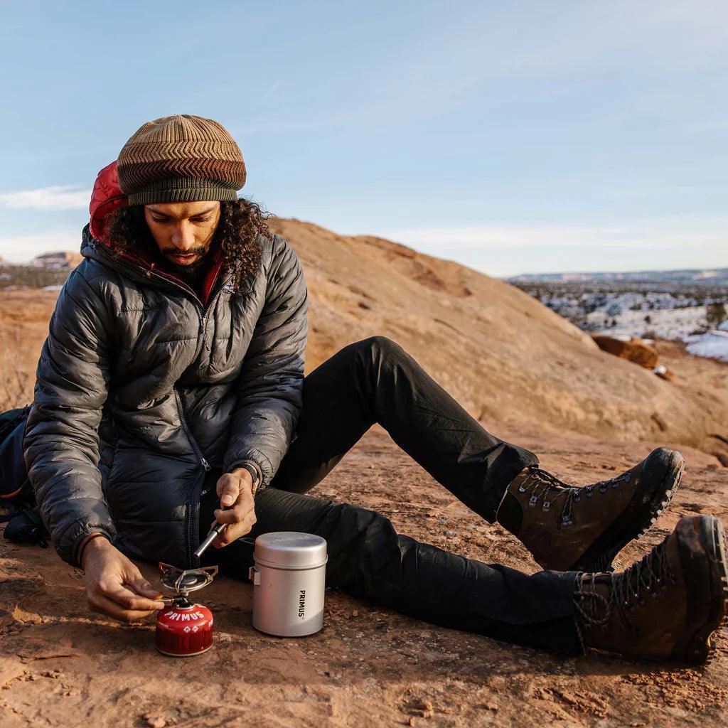 Camper using Primus trail kit backpacking stove on rocky outdoor terrain