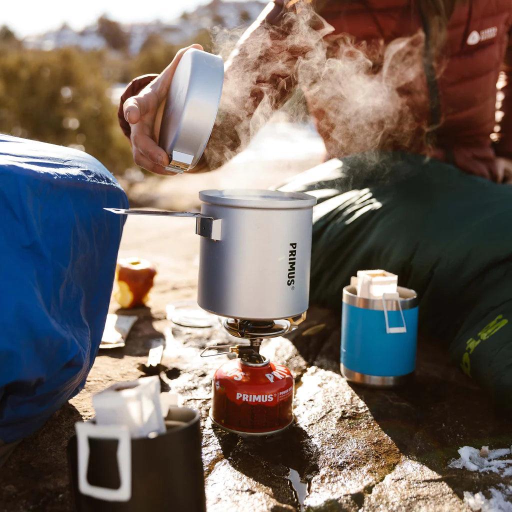 Primus backpacking stove cooking kit with steaming pot outdoors on a rocky campsite