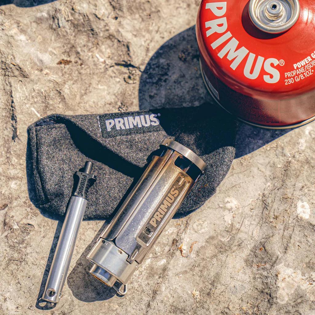 Primus backpacking stove, fuel canister, and case on rocky surface outdoors