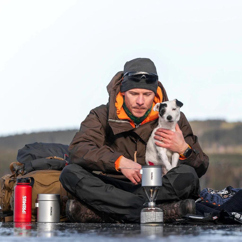 Camper with dog using Primus Firestick backpacking stove outdoors