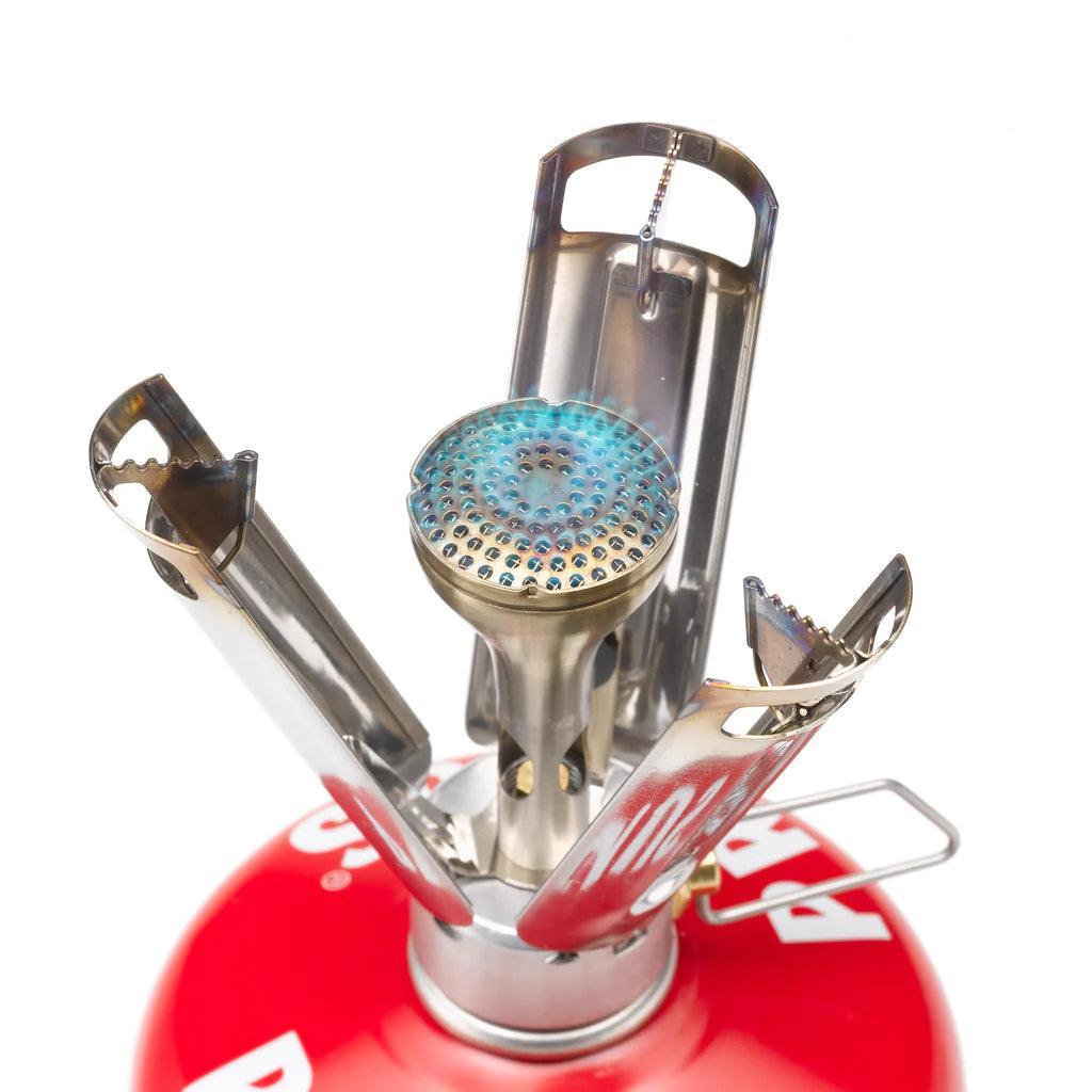 Primus Firestick backpacking stove with lit blue flame on red fuel canister, white background