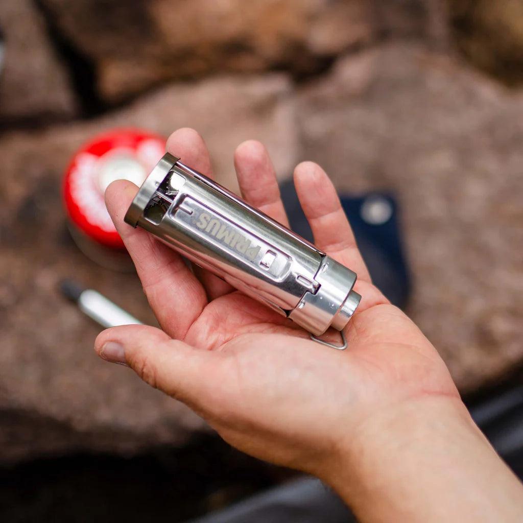 Primus Firestick backpacking stove held in hand outdoors on rocky surface