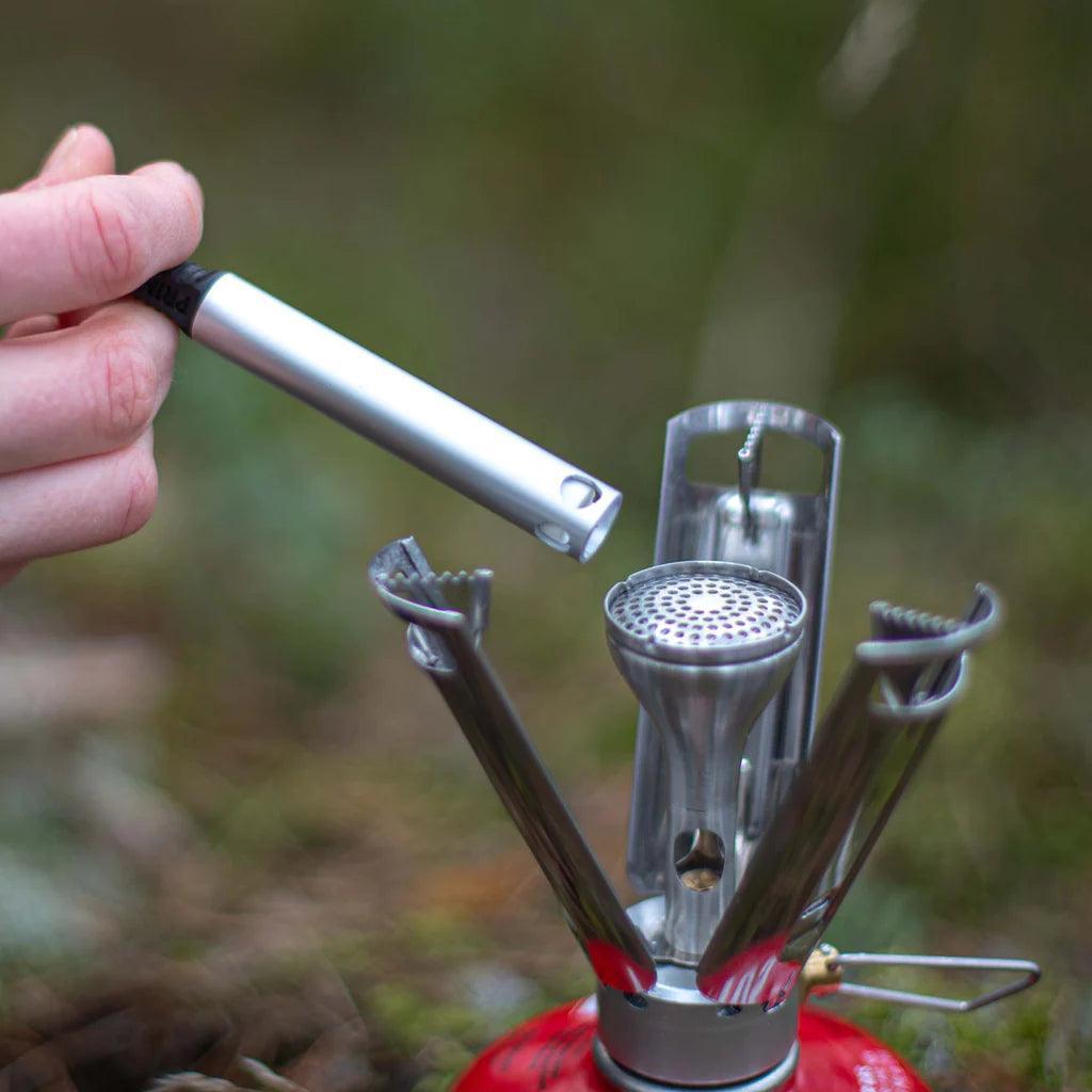 Hand holding igniter next to Primus Firestick backpacking stove outdoors