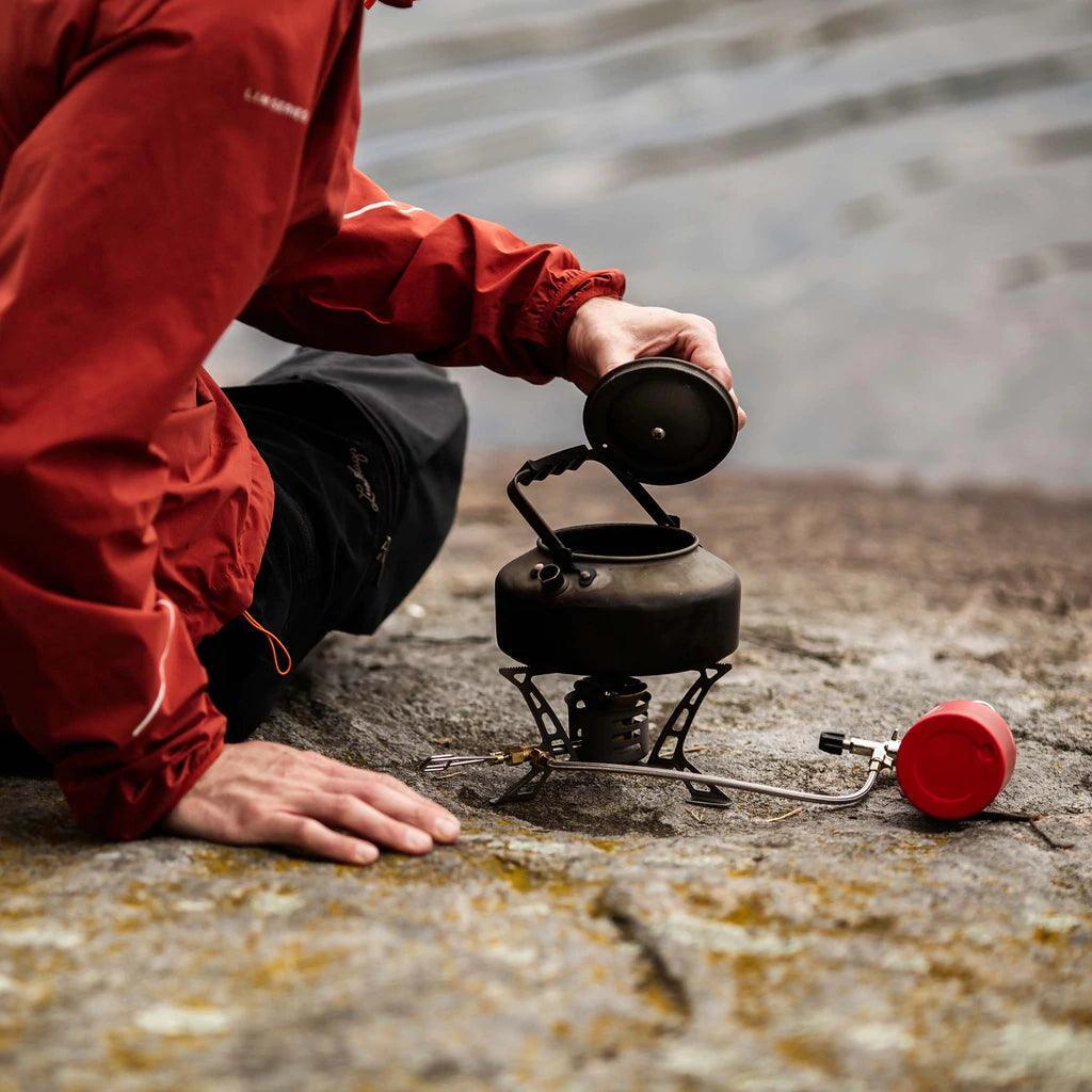 Camper in red jacket using a Primus Litech coffee tea kettle on a portable stove outdoors