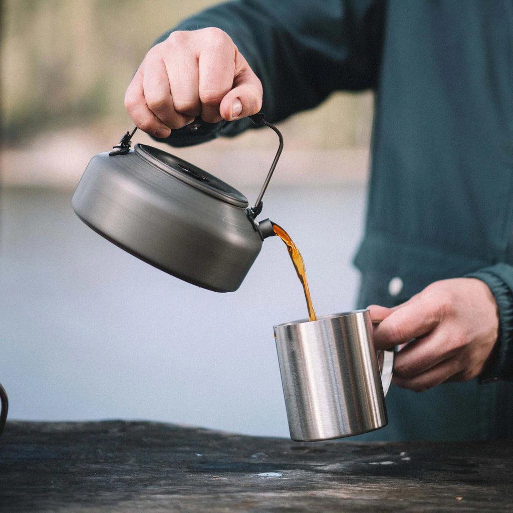 Person pouring coffee from a Primus Litech camping kettle into a metal mug outdoors