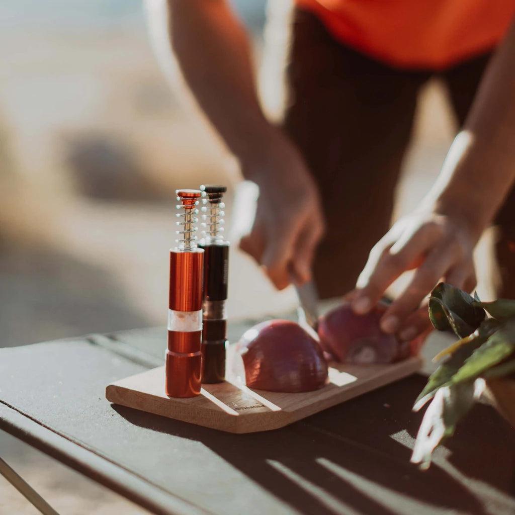 Primus campsite salt and pepper mill set on cutting board with chopped onions outdoors