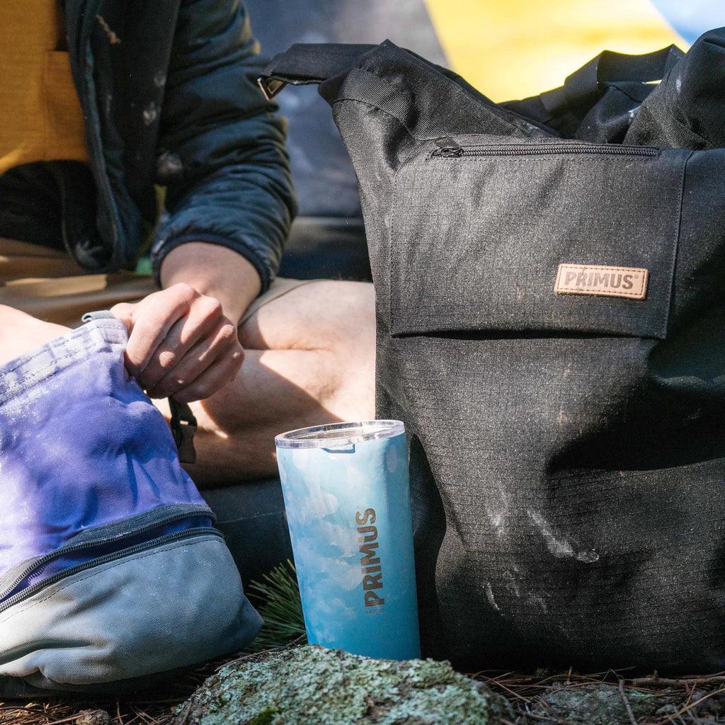 Primus cooler backpack and tumbler outdoors with person sitting nearby