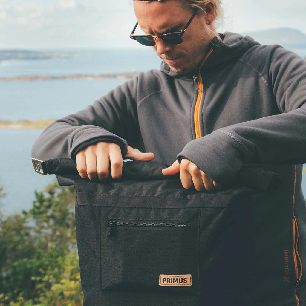 Man in outdoor gear opens Primus cooler backpack with scenic lake view