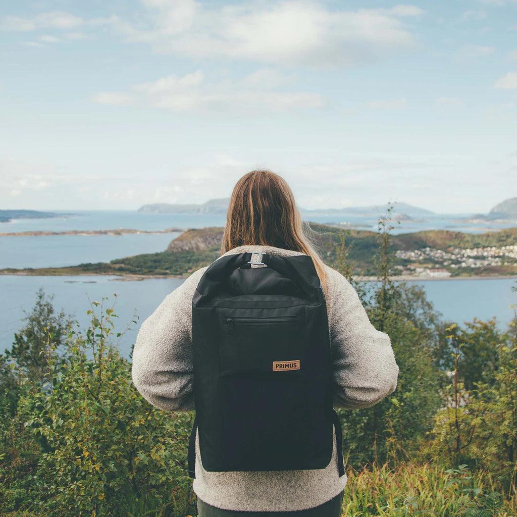 Person wearing Primus cooler backpack overlooks scenic outdoor landscape with water and hills