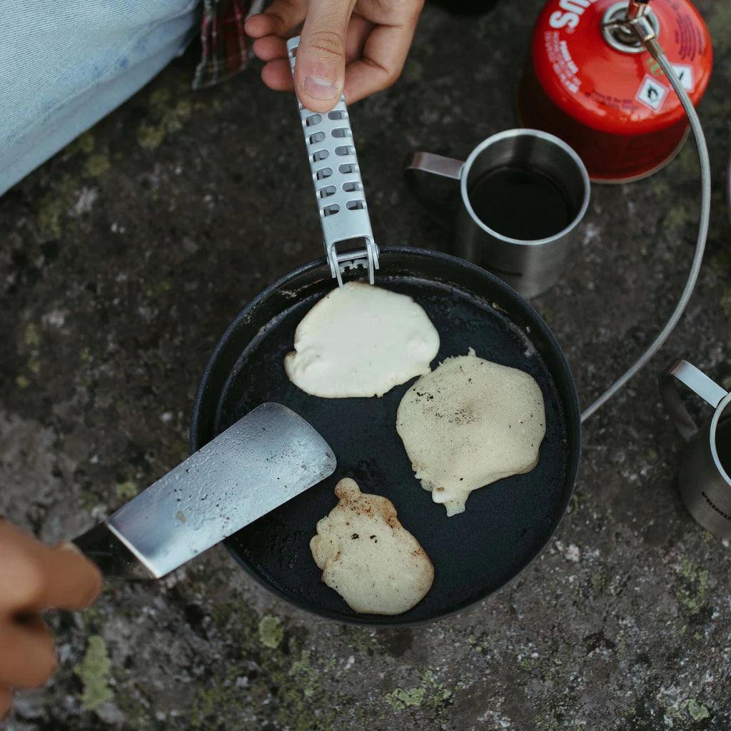 Camp cooking pancakes in Primus Essential Pot Set with a spatula and mugs outdoors