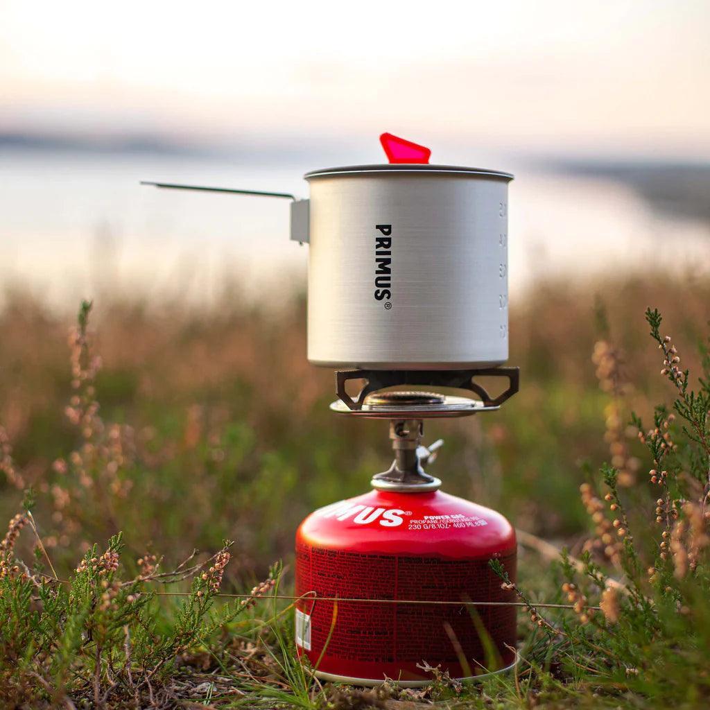 Primus camping stove and trek pot on red fuel canister outdoors on grass