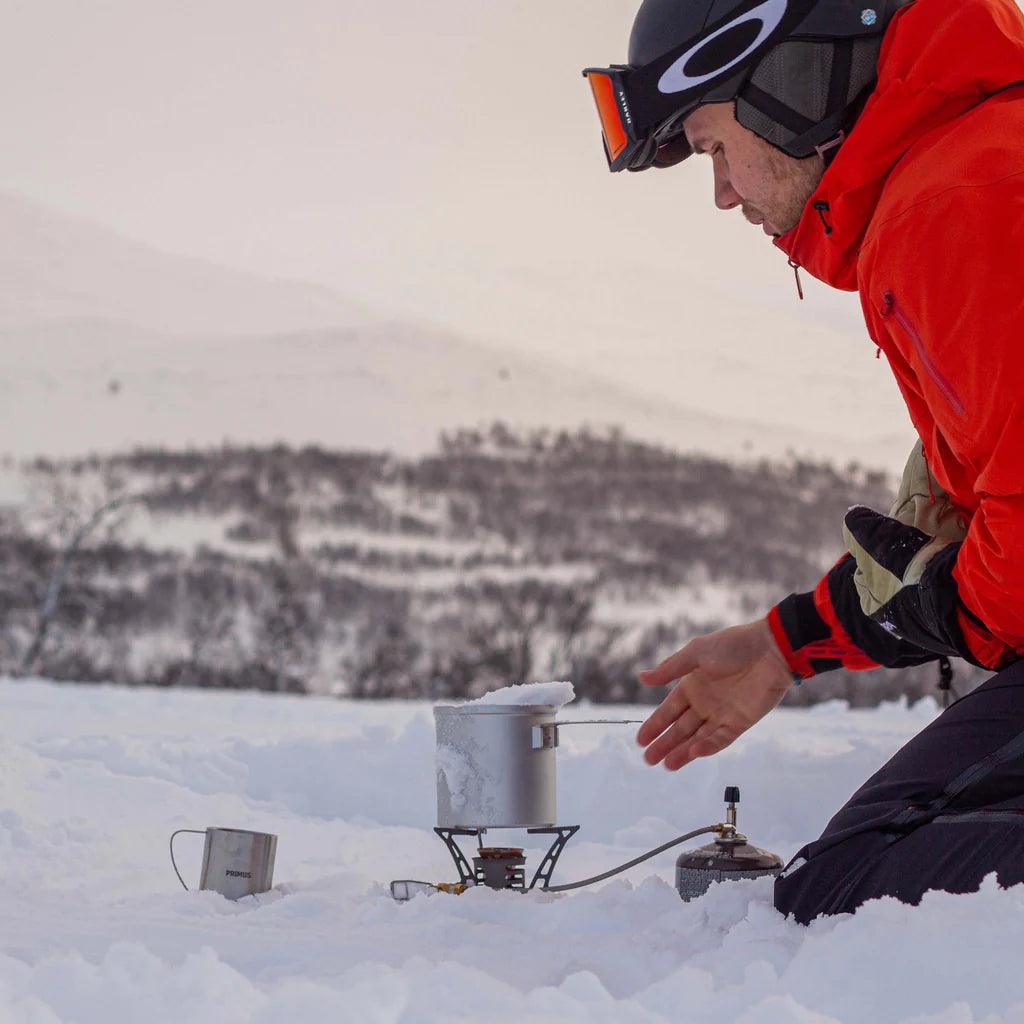 Man in winter gear using Primus Essential Trek Pot on a portable stove in snowy outdoors