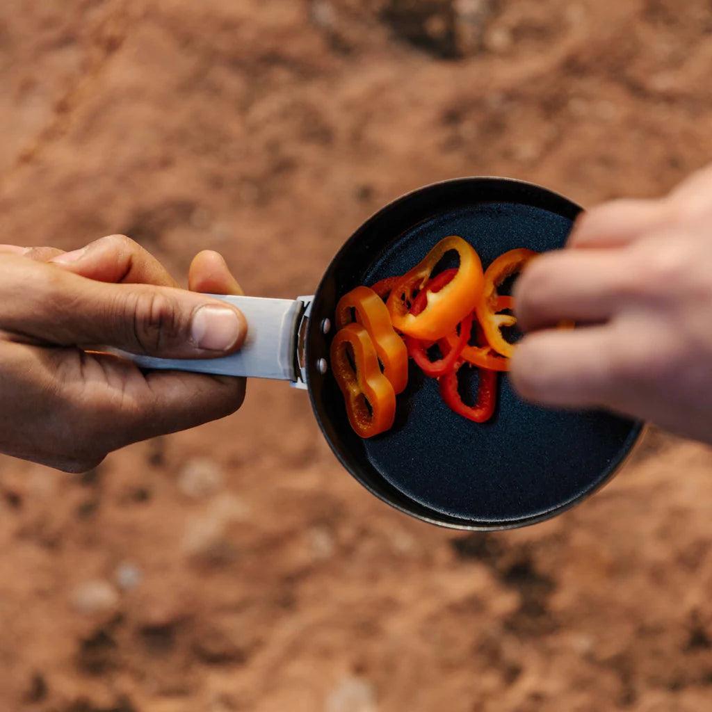 Person holding Primus Essential Trek Pot with sliced peppers outdoors