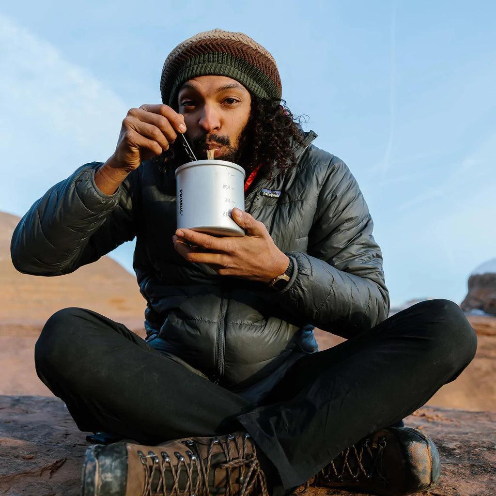 Man in outdoor gear eating from Primus Essential Trek Pot on rocky terrain