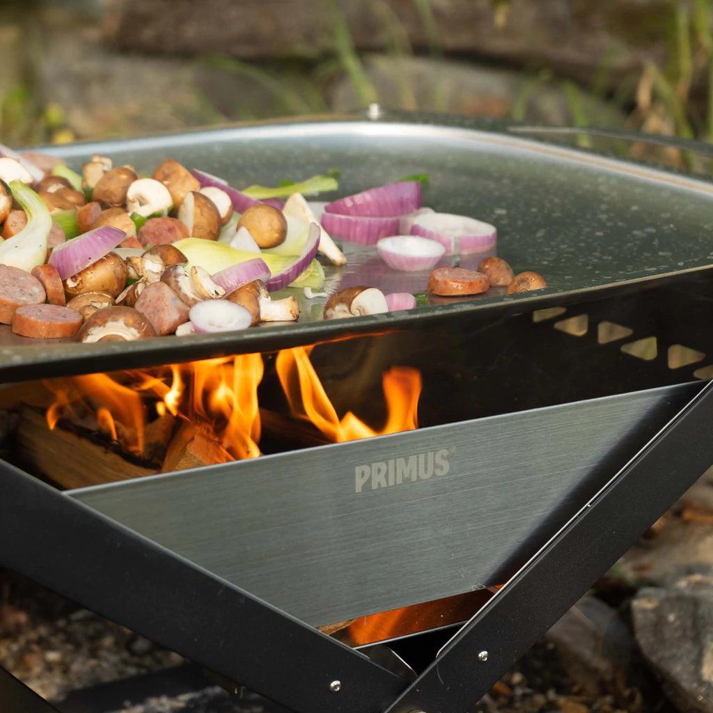 Primus Kamoto open fire pit grill with vegetables and sausage cooking outdoors