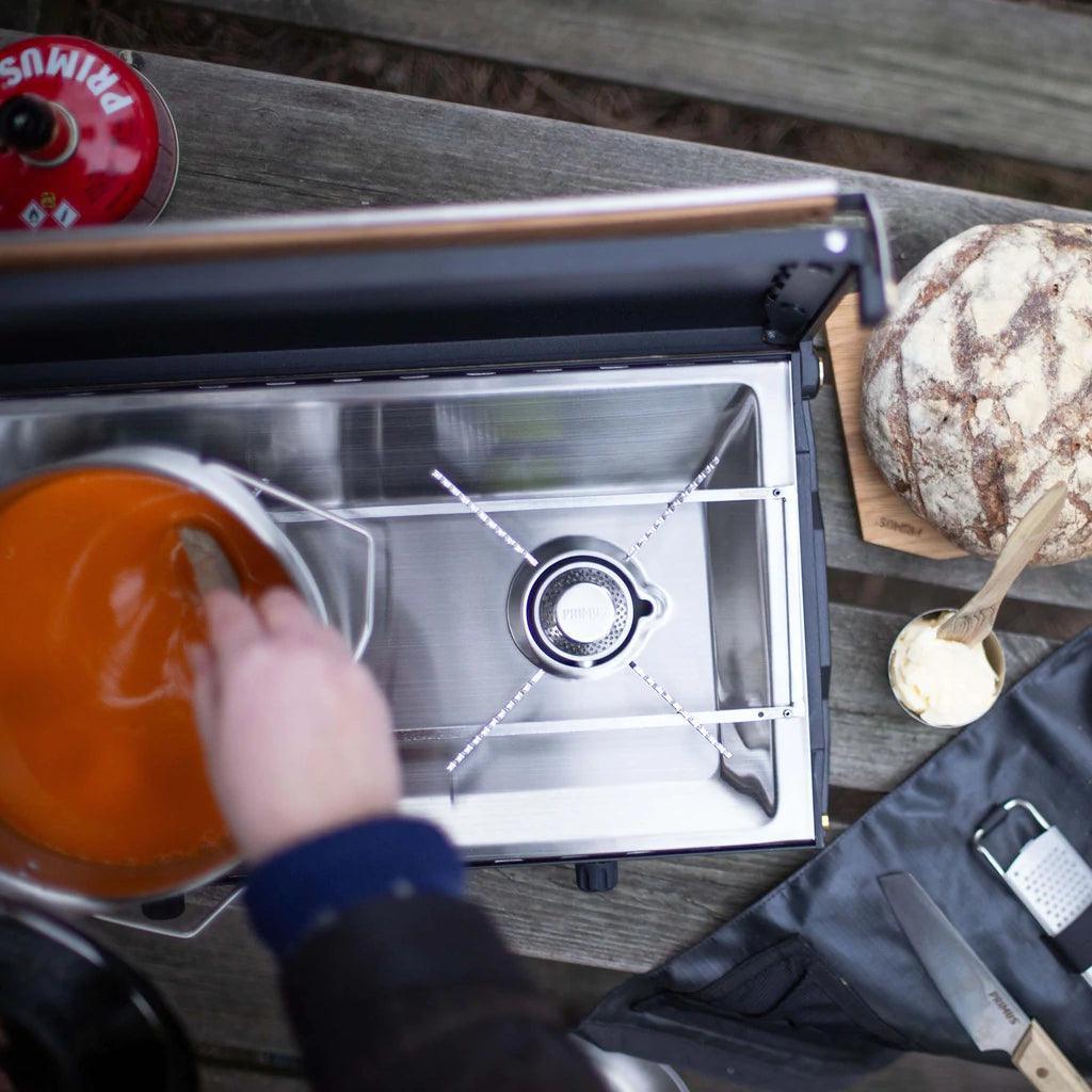Primus Kinjia camping stove in use outdoors with soup pot, bread, and butter on a wooden table