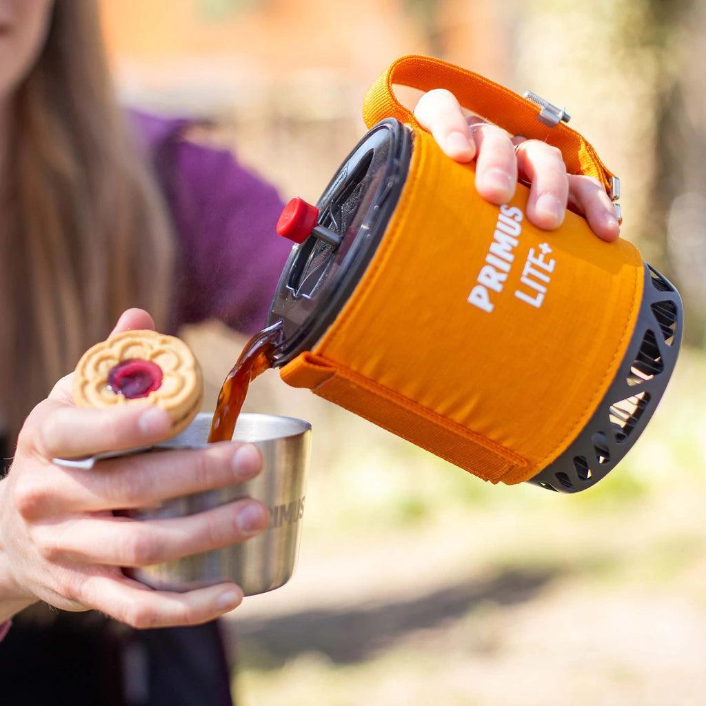 Primus Lite Plus stove system pouring hot drink outdoors into a metal cup with a cookie
