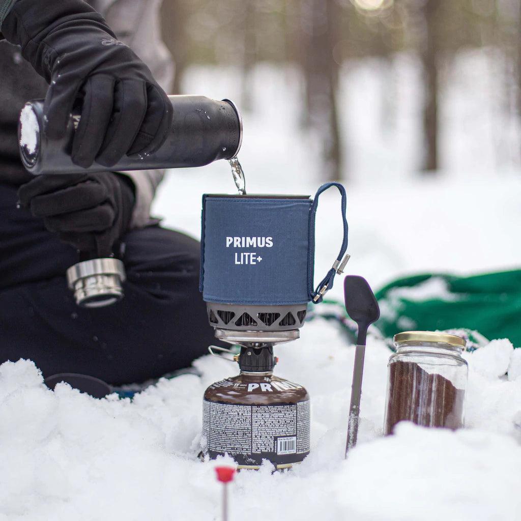 Primus Lite Plus stove system heating water on snow, outdoor winter camping scene