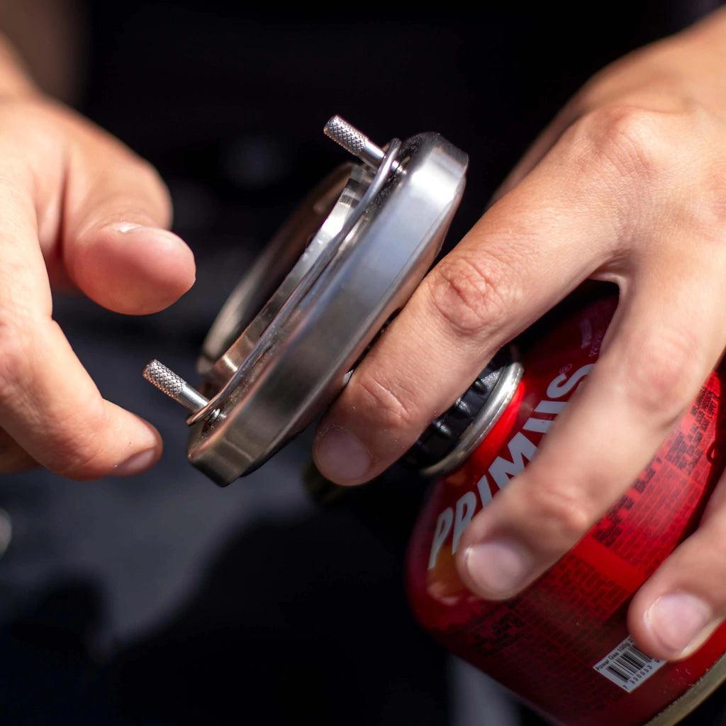 Hands assembling Primus Lite Plus camping stove system with red fuel canister outdoors