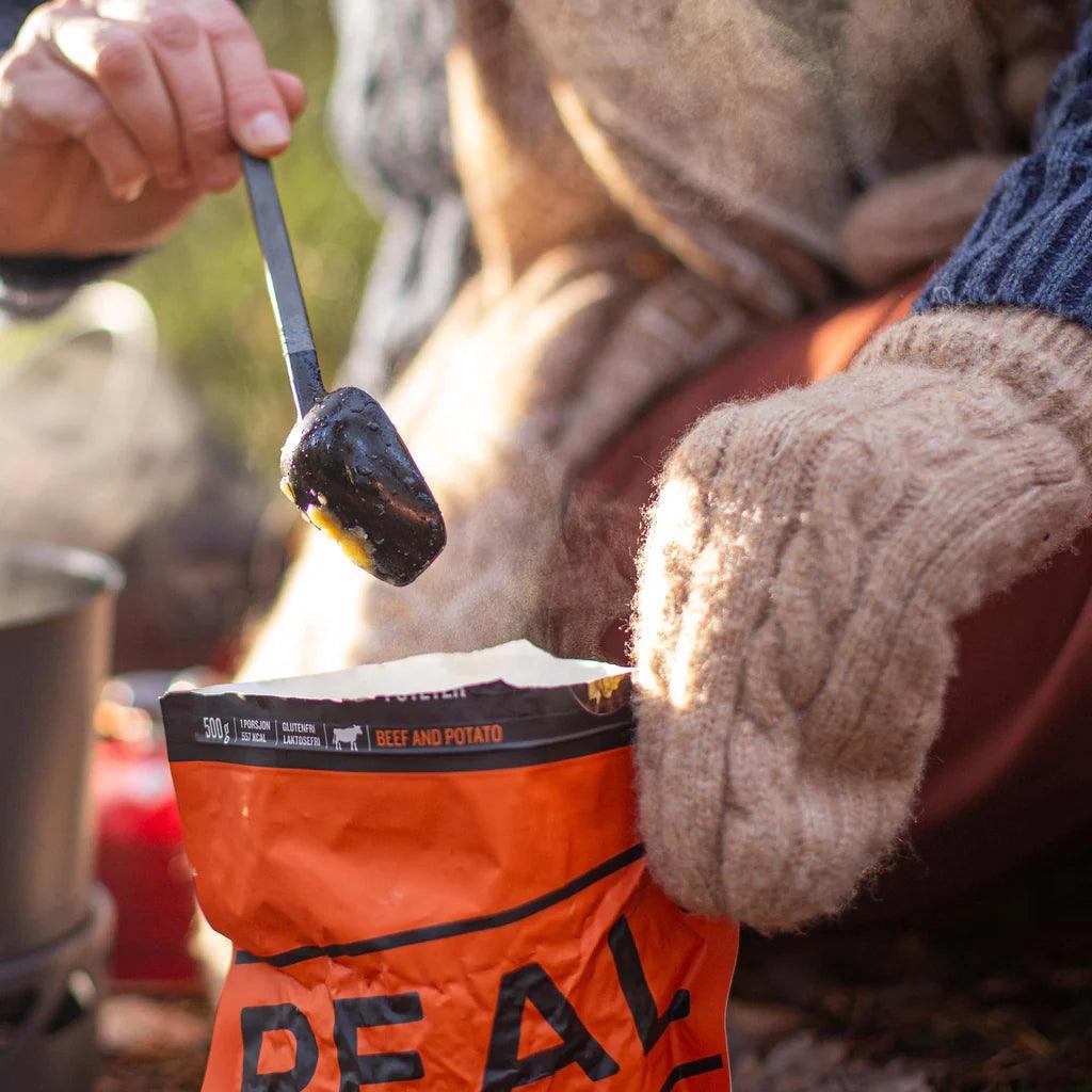 Primus long spoon scooping hot beef and potato meal outdoors, person wearing knit mittens